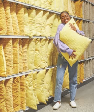 Image of a woman holding a yellow pillow next to a stand of yellow pillows.