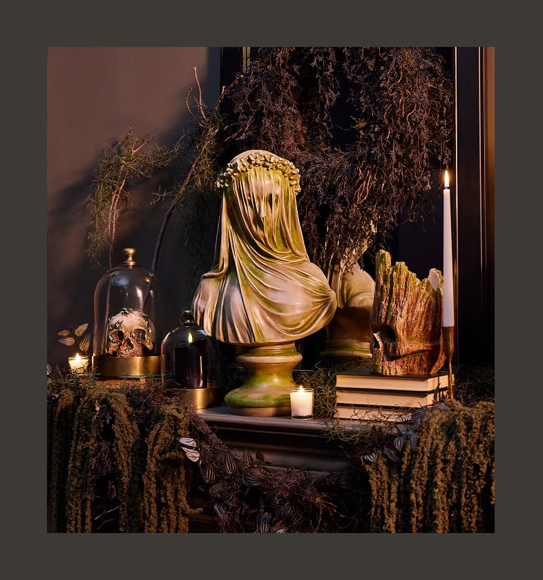 Grim Gardens Halloween decor with a draped bust, skull, candles, and moss