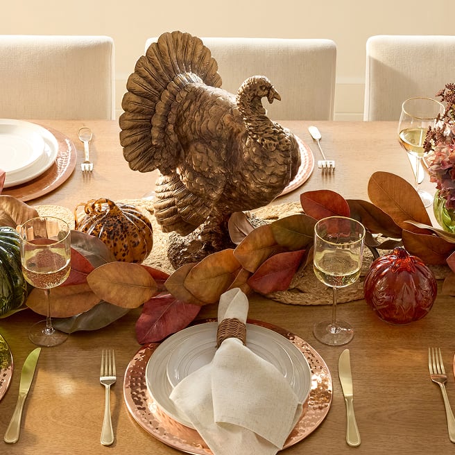 Thanksgiving table with a turkey centerpiece, glass pumpkins and fall foliage