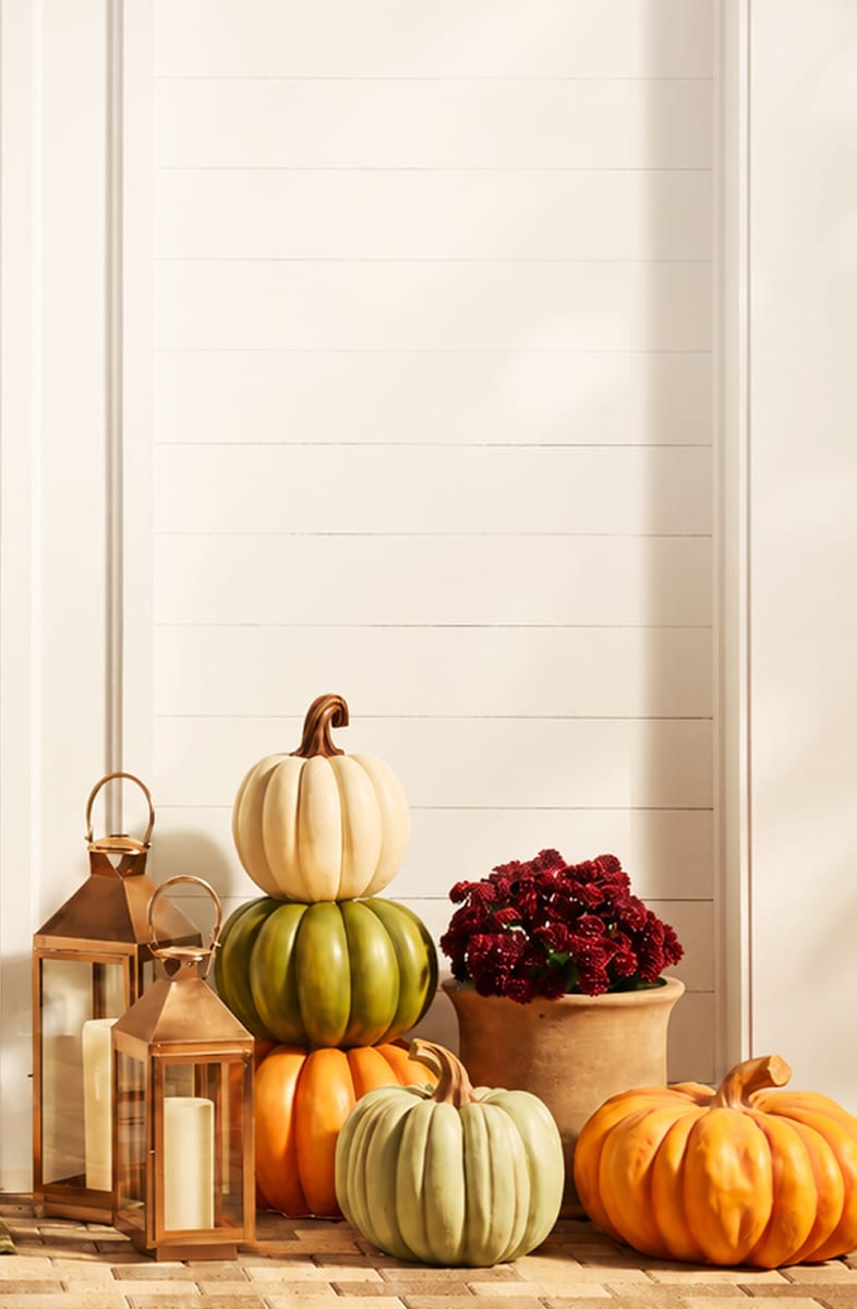 Fall porch decorated with stacked pumpkins, lanterns, mums and a seasonal sign