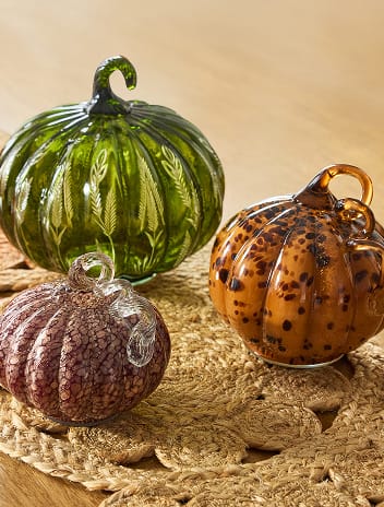 Green, amber and brown glass pumpkins on woven mats